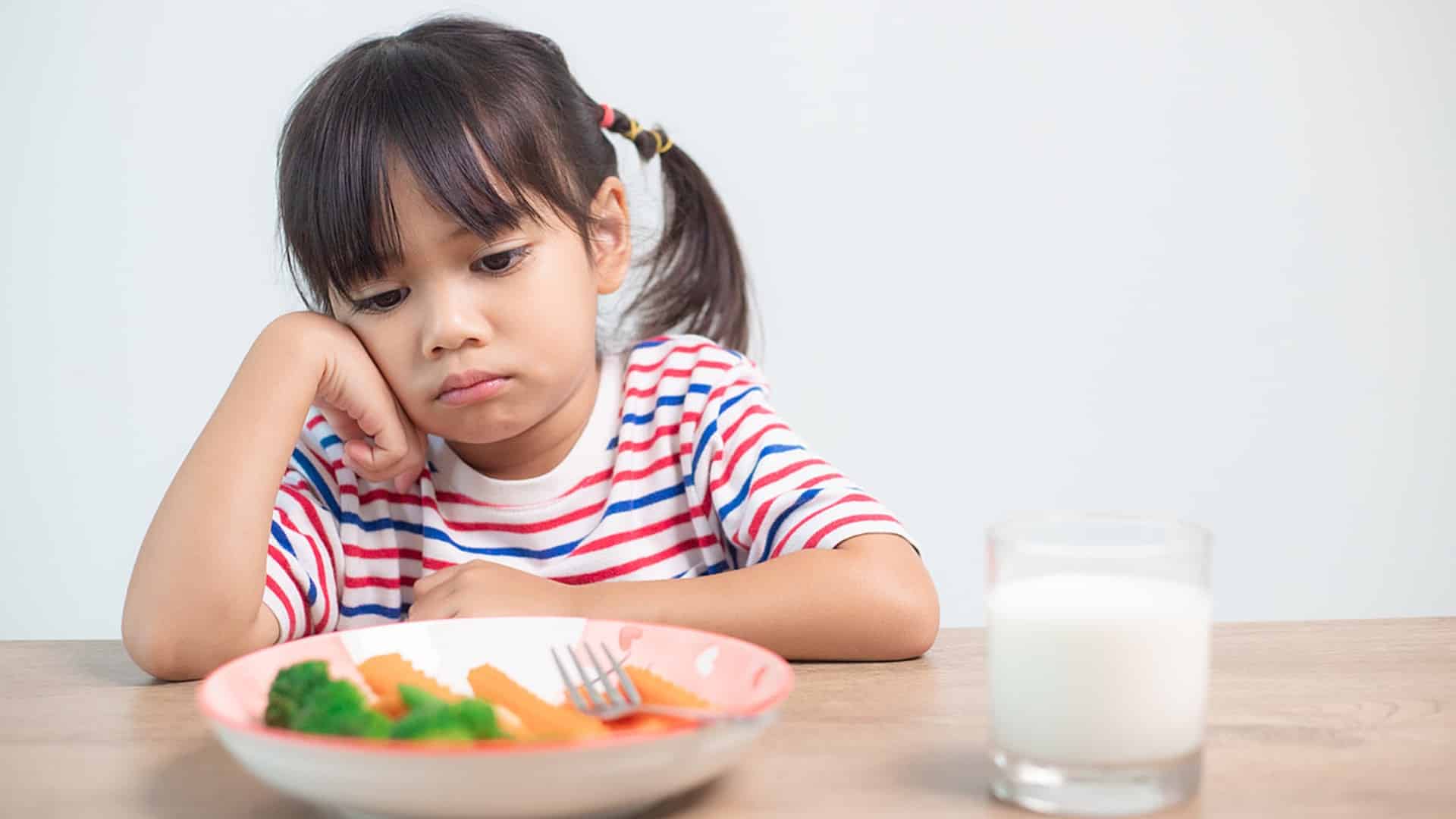 A young girl looks at a plate with food on it with disinterest