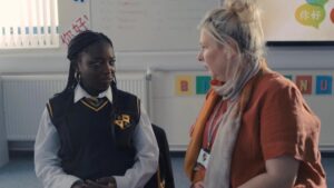 Girl in a uniform talks to a teacher in a classroom. From the Netflix series "Adolescence".
