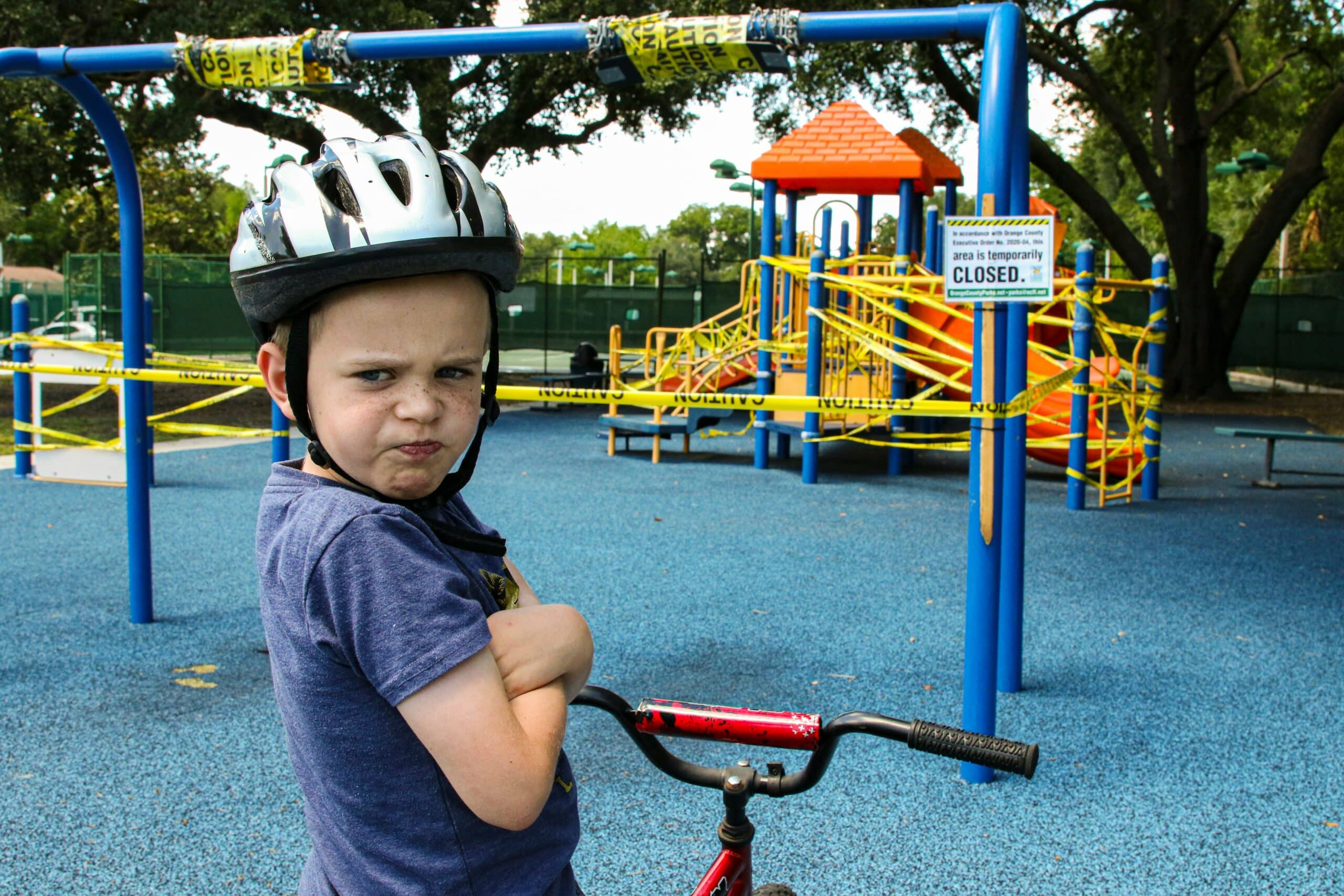 Angry child on a bike next to playground with no entry tape