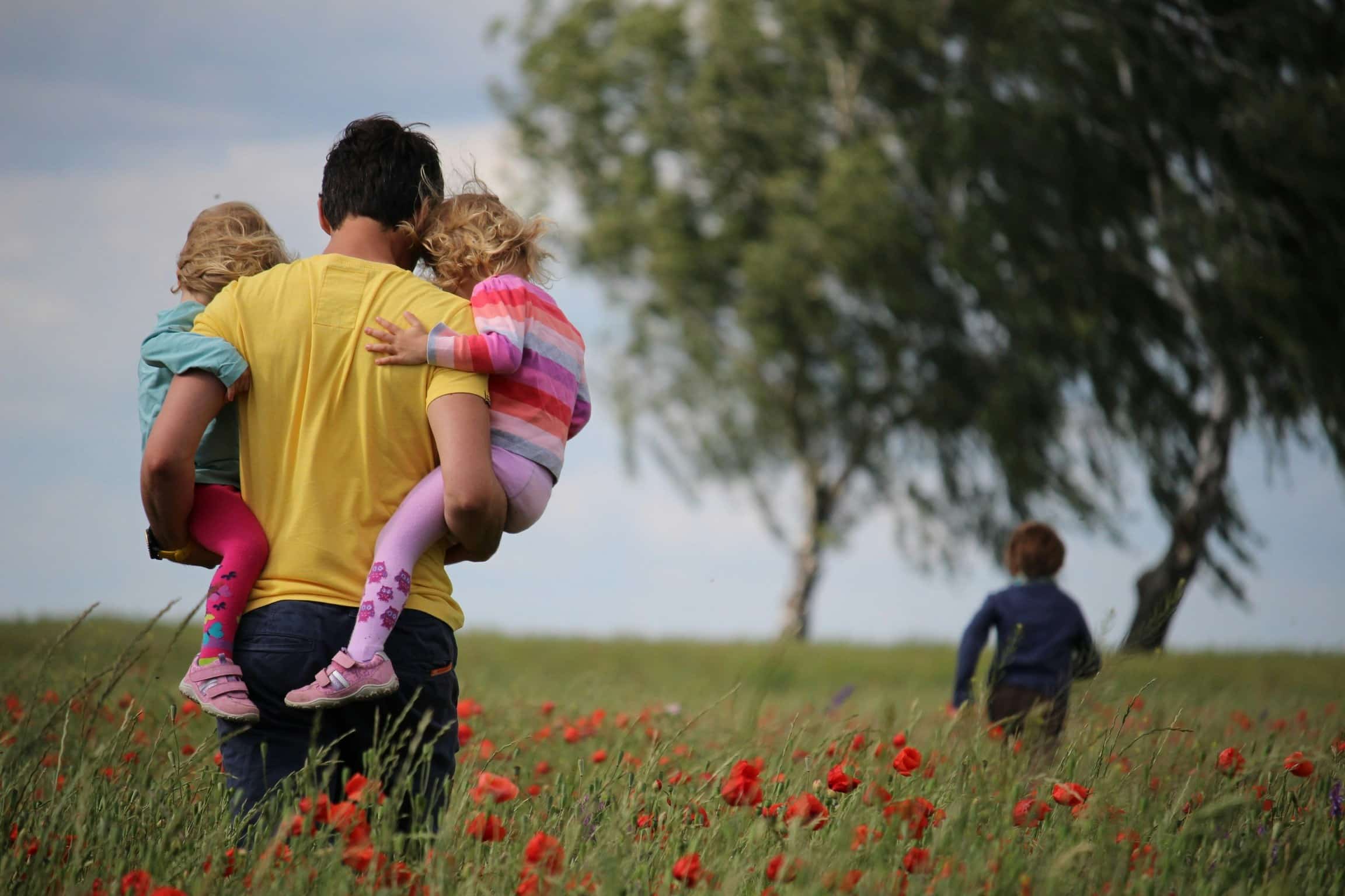Father carrying children across a field n sunny weather.